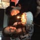A young woman and a young man with cerebral palsy sit together while smiling at a large white birthday cake with candles.